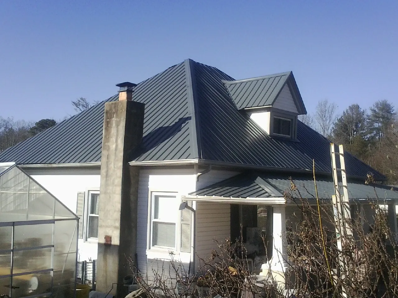 Dark blue standing seam metal roof on a white farmhouse with dormer — Slate & Tile Roof Repair by Roofing Brothers in Maquon