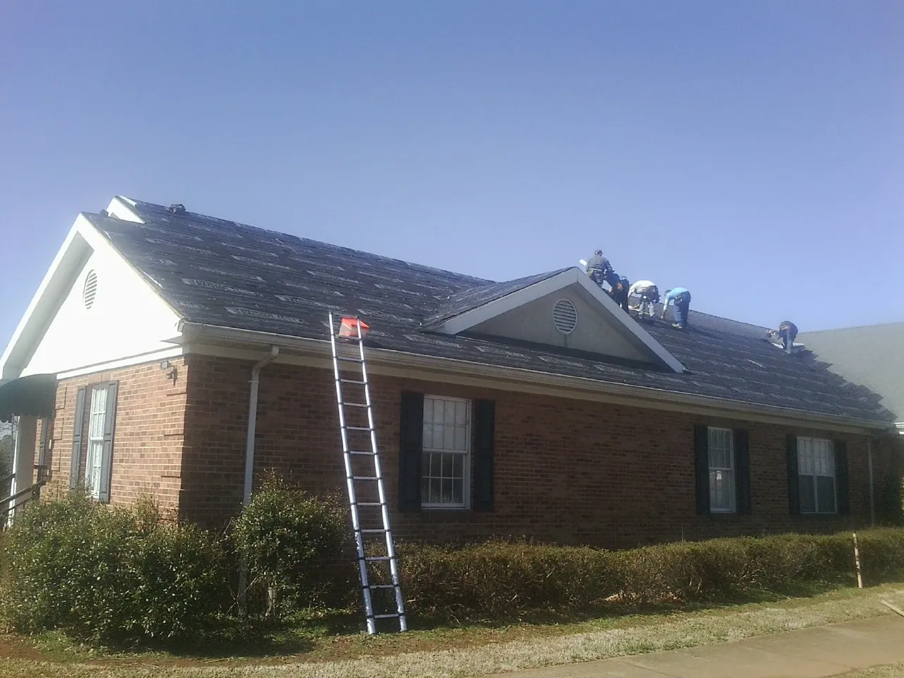 Crew tearing shingles off a brick ranch roof with a ladder set — Metal Roof Repair work by our crew in Maquon