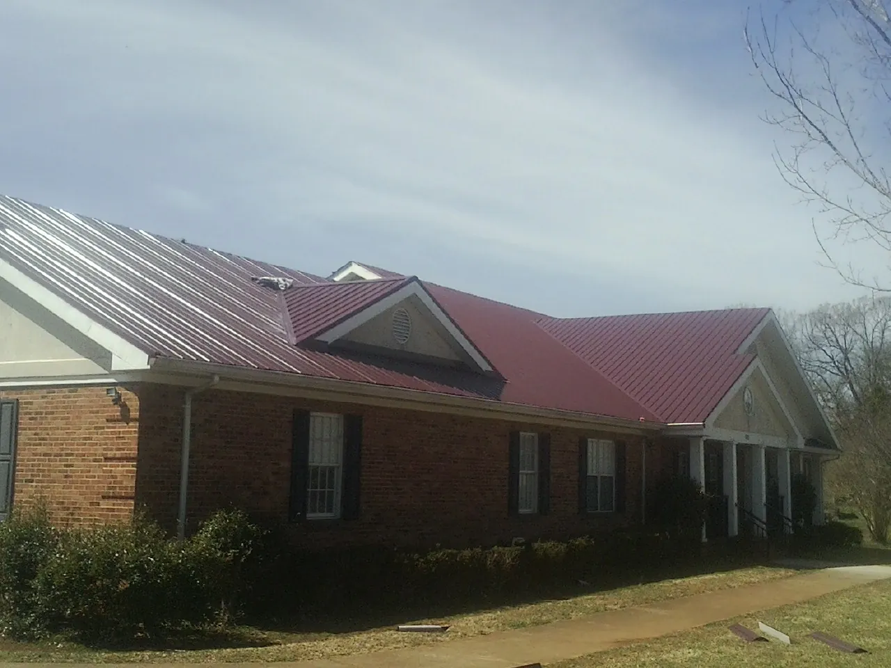 Red metal roof with gabled entries on a long brick building, from a Hail Damage Roof Repair job in Maquon