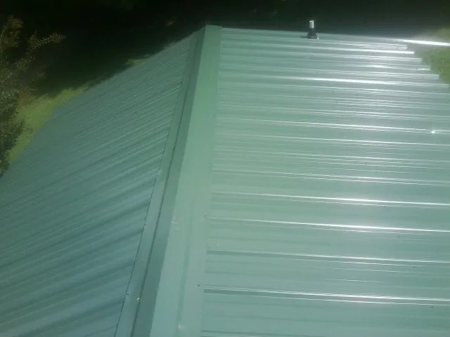 New green metal panels meeting at the ridge of a roof — Flat Roof Repair work by our crew in Maquon