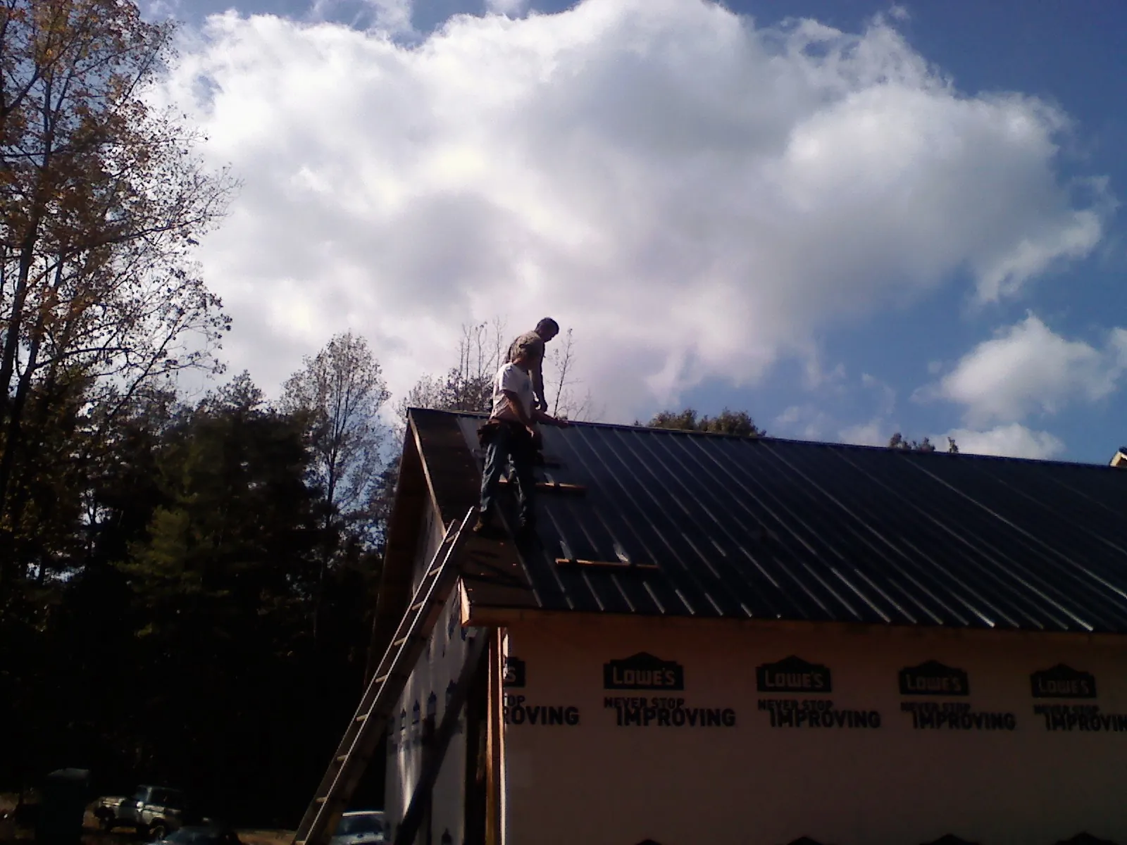 Roofer fastening dark metal panels high against a cloudy sky, from a Roof Inspection job in Maquon