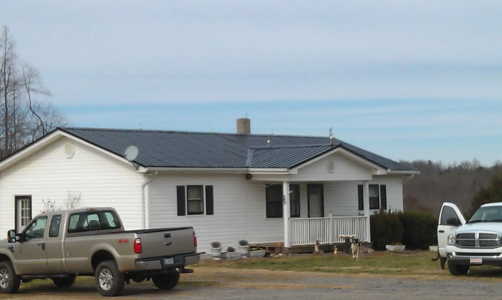 Finished dark metal roof on a white ranch home with work trucks parked in Maquon