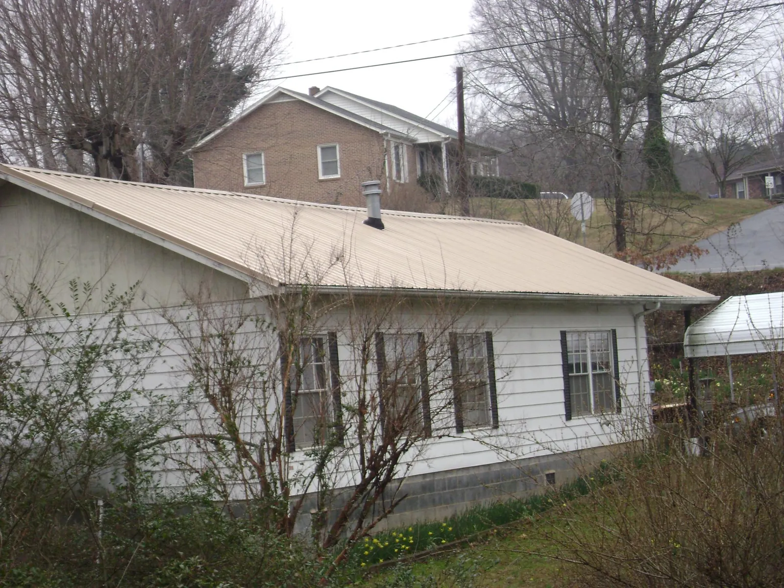 Tan metal roof on a white sided house set into a hillside — Commercial Roofing by Roofing Brothers in Maquon